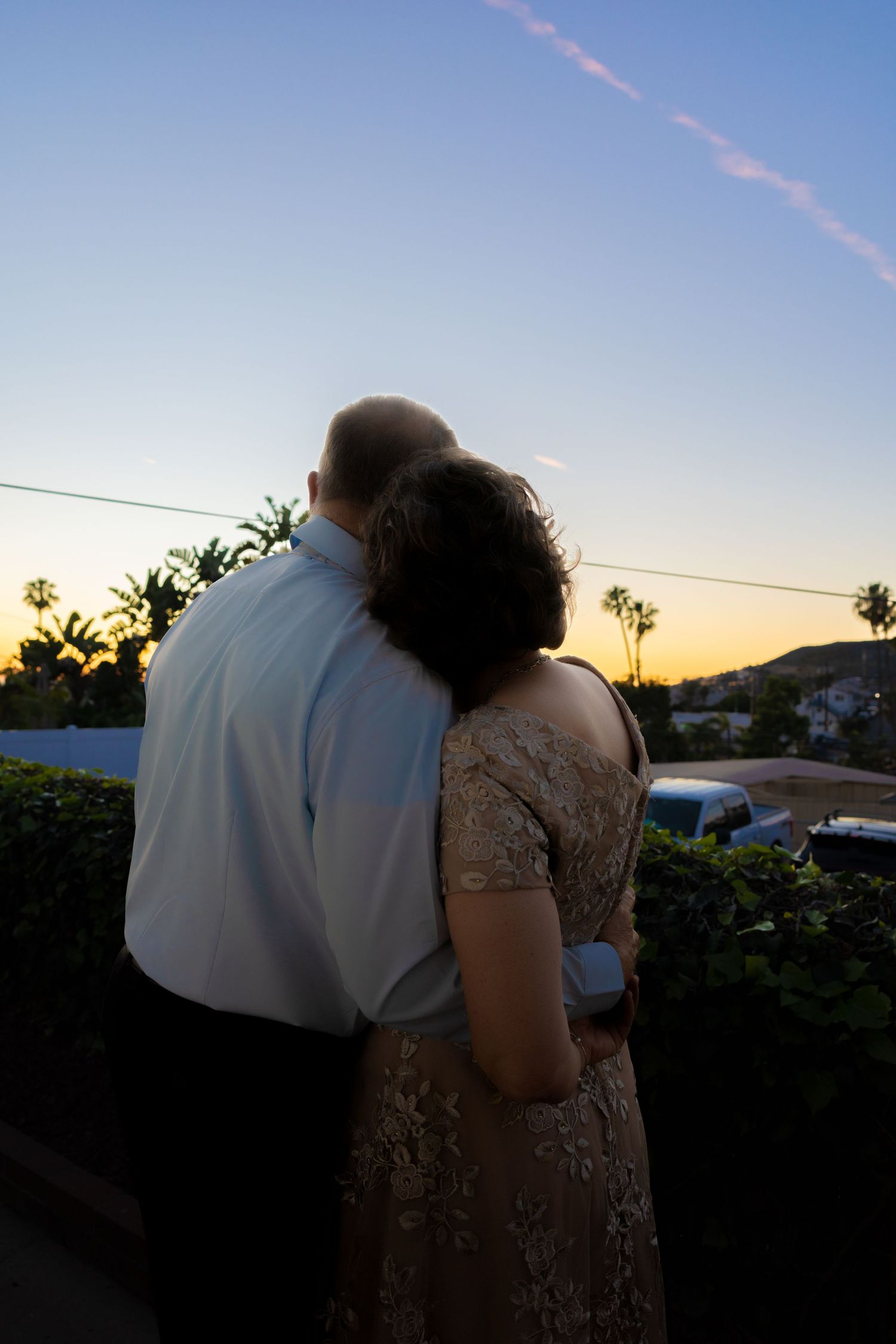 Couple embracing at sunset with palm trees and hills in the background during an outdoor evening event.