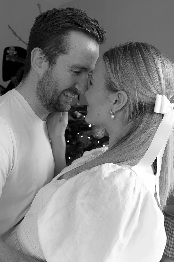 An intimate black and white portrait of a couple sharing a tender moment by the Christmas tree.
