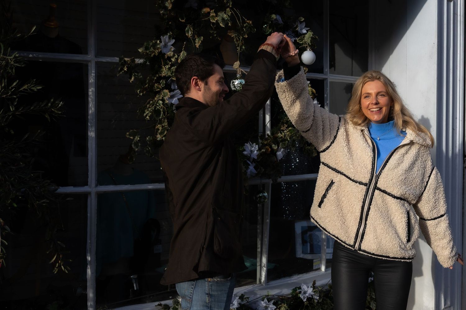 A romantic winter scene with holiday decorations and a couple sharing an intimate moment by a decorated doorway.