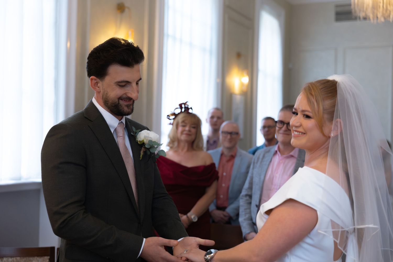 Bride and groom exchanging rings at elegant wedding ceremony with guests in background.