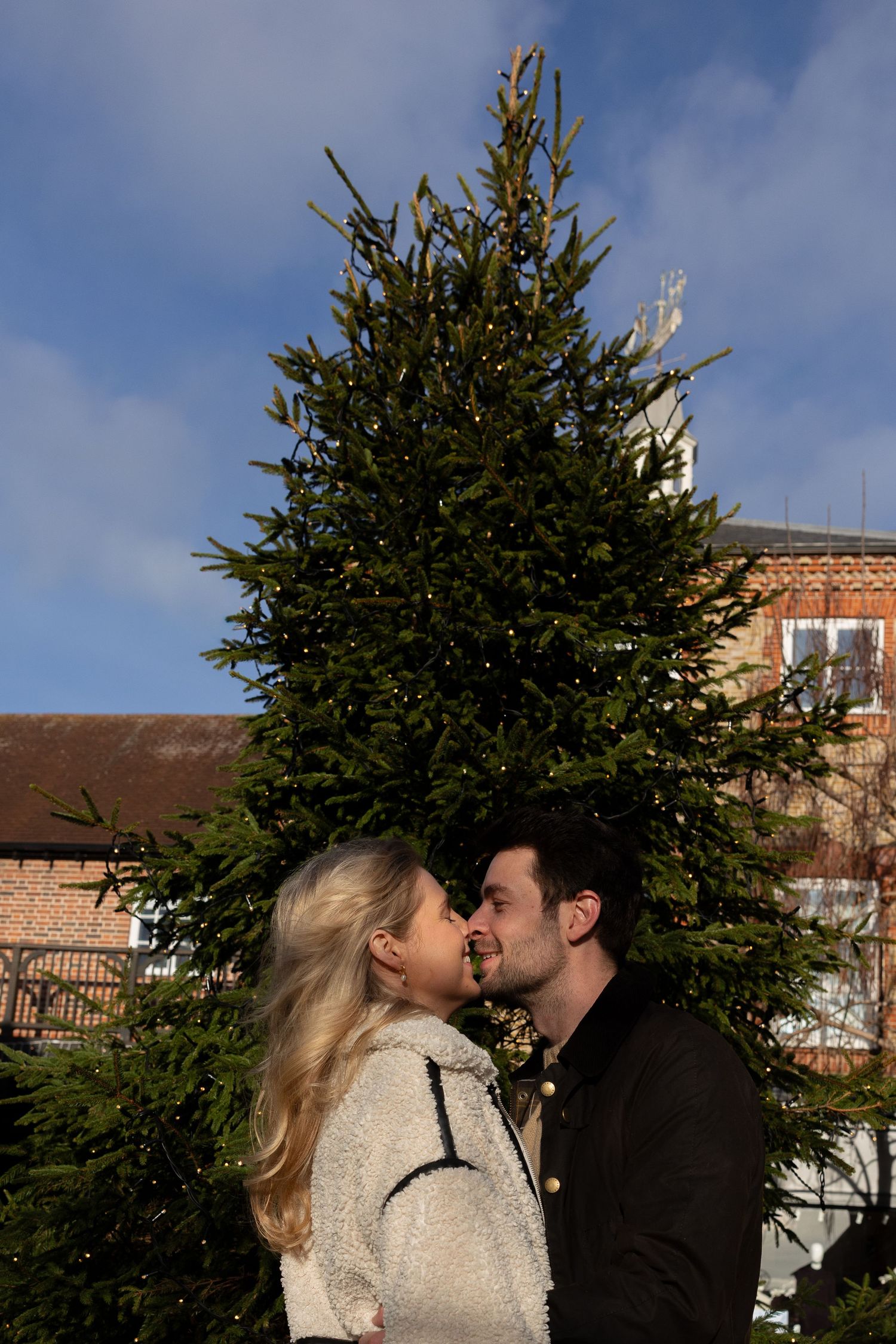A winter romance scene with evergreen trees and brick buildings in the background.