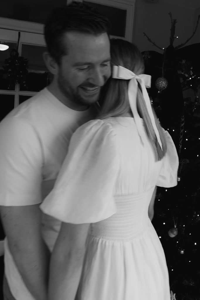 A couple in white sharing a romantic moment with a decorated Christmas tree in the background.