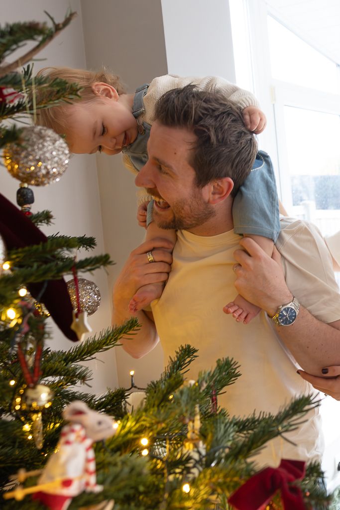 A playful moment by the Christmas tree as a child rides on shoulders while decorating.