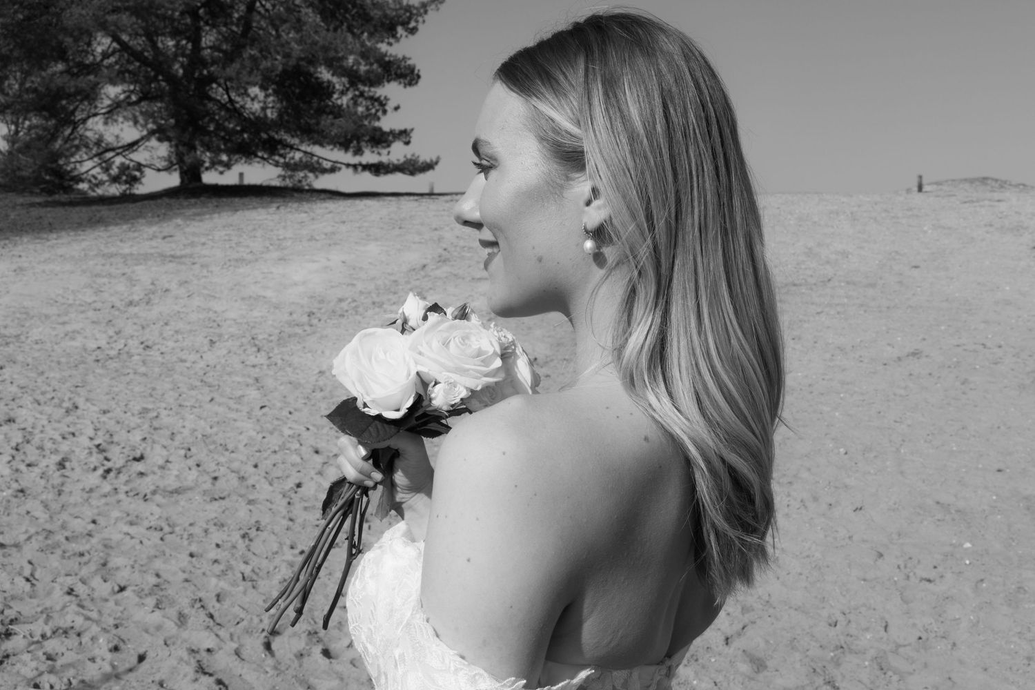 Black and white photo of a smiling bride holding a bouquet of roses on a sandy beach.