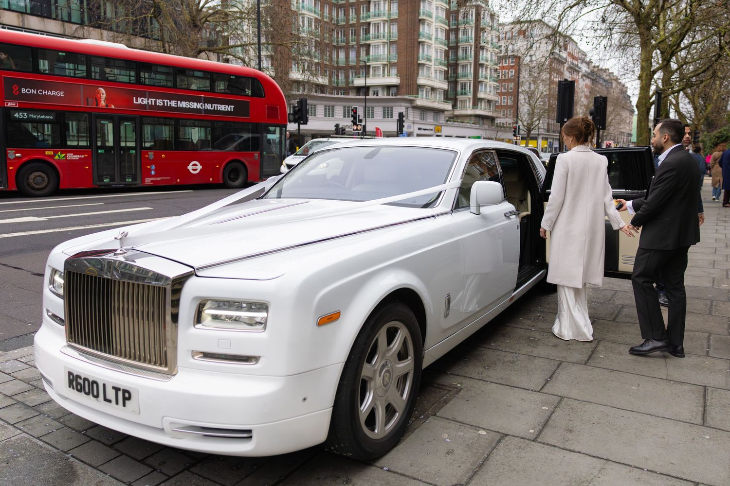 White Rolls-Royce Phantom wedding car parked on London street with red double-decker bus.