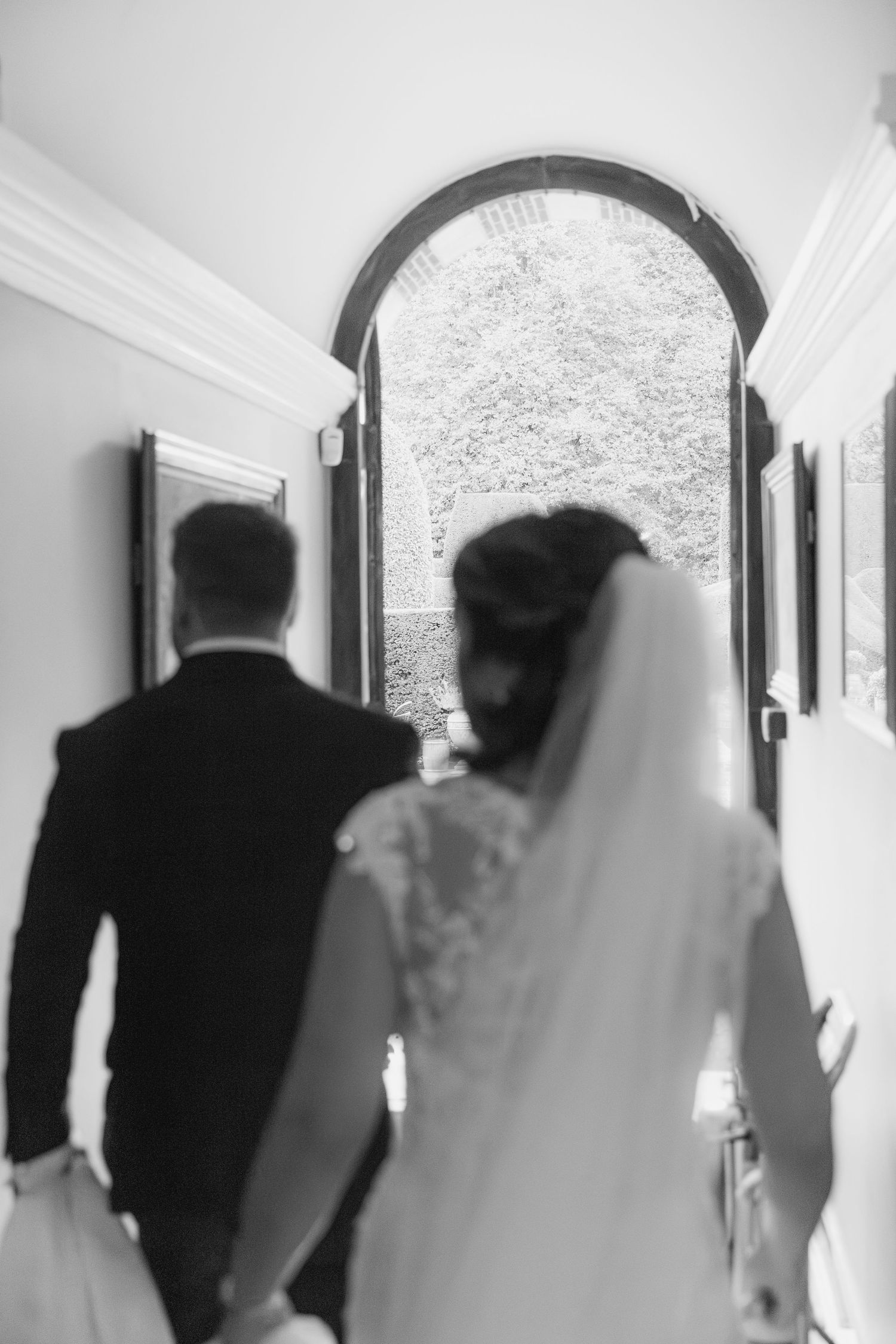 Silhouettes of a wedding couple walking through arched doorways in a hallway.