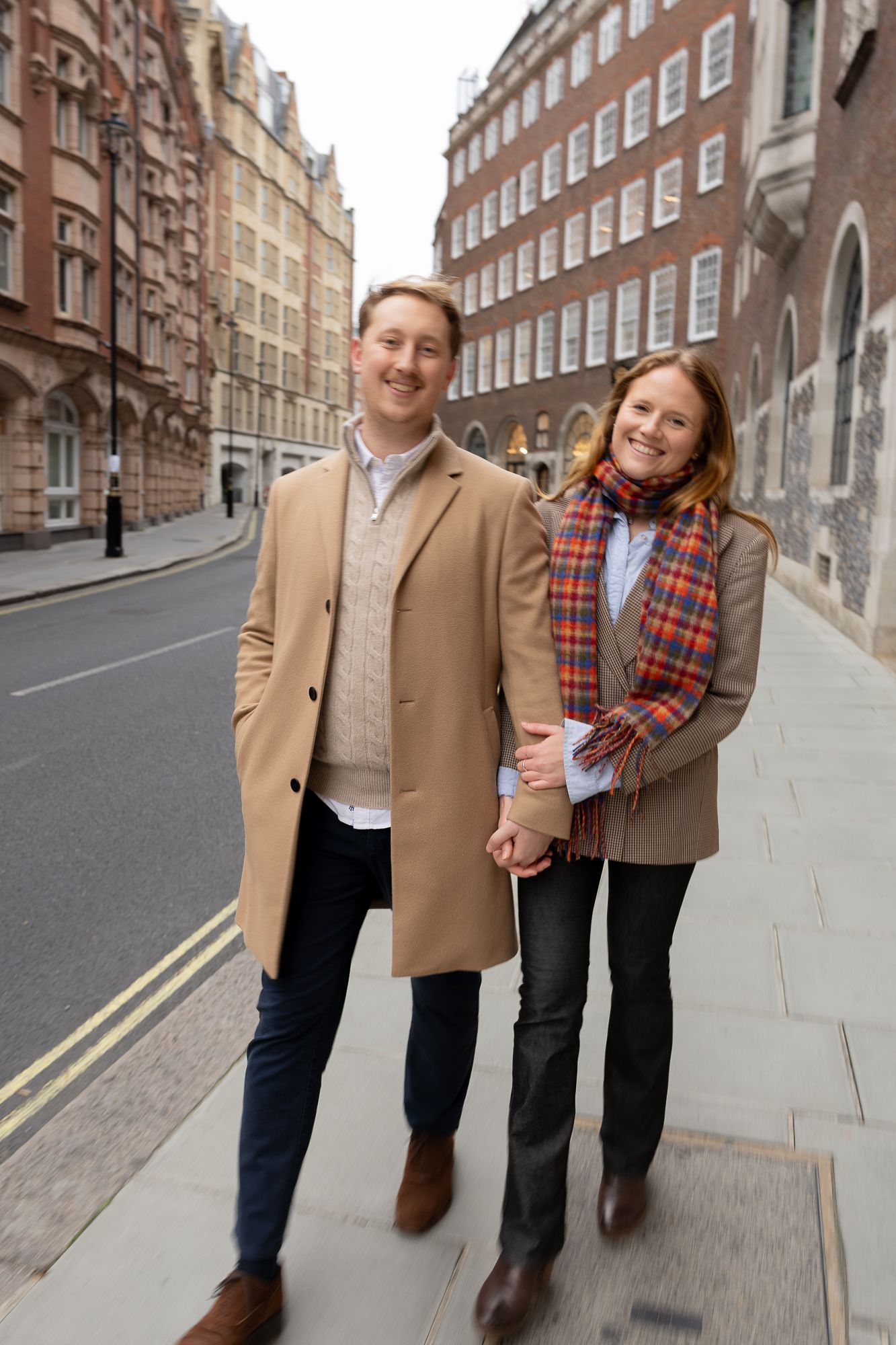 A happy couple walks hand in hand down a historic street in winter clothing.