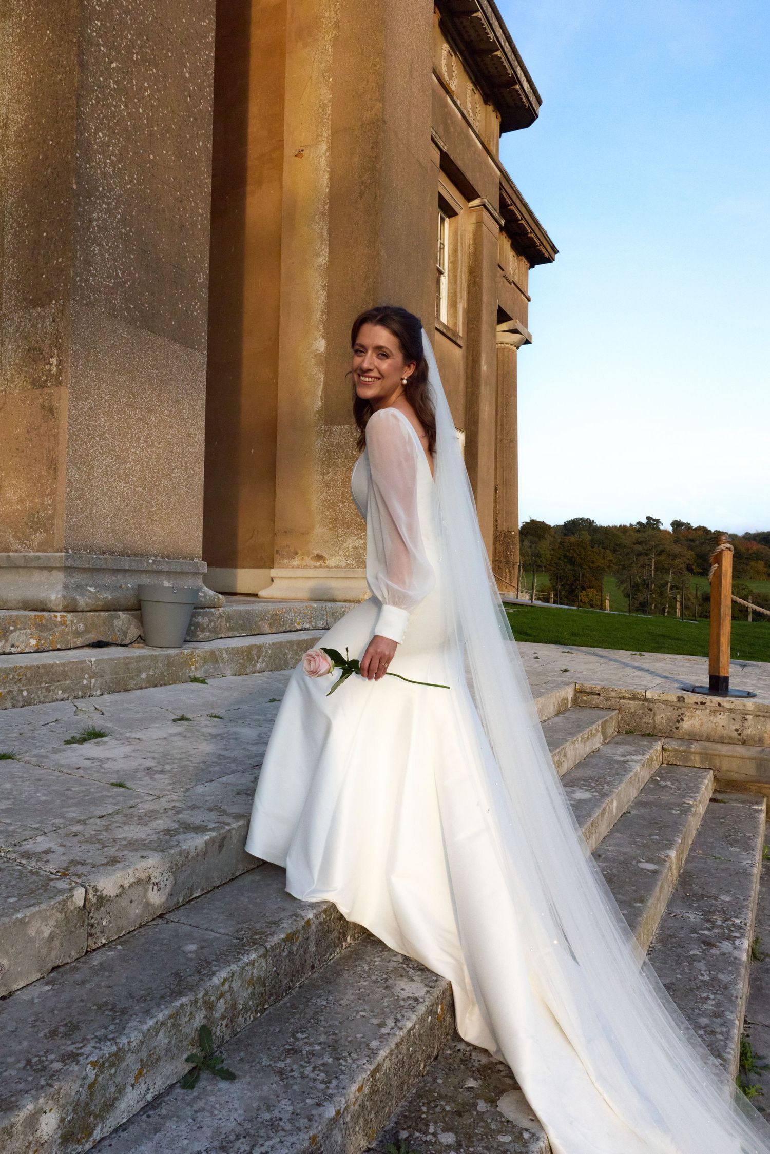 Bride's white dress and veil flow gracefully on stone steps of a historic building.