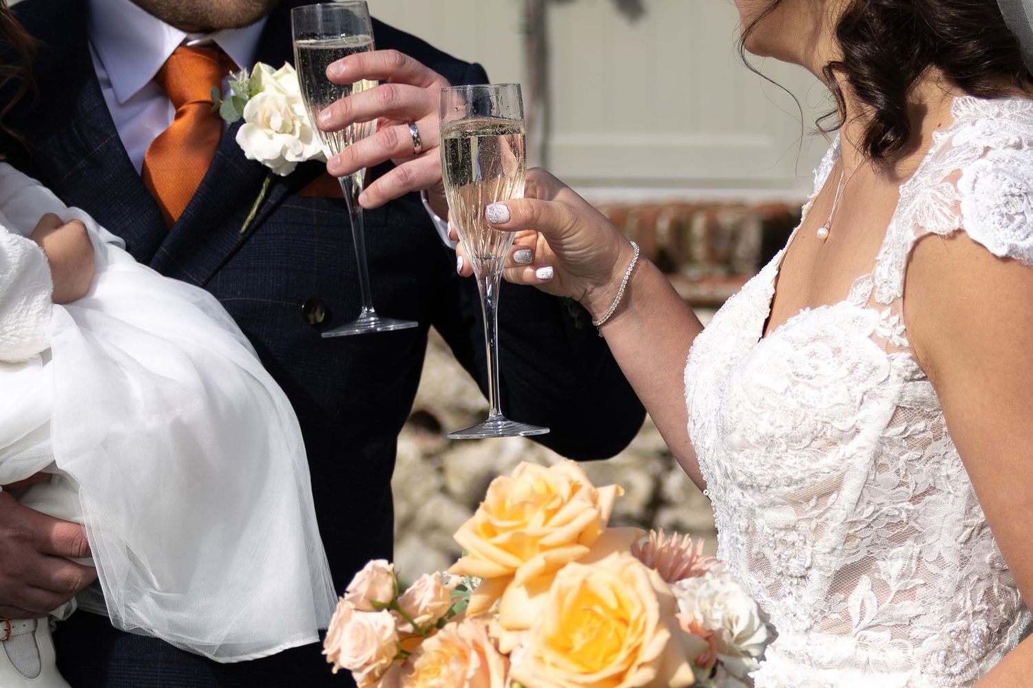 Two people toast with champagne glasses at a wedding reception with yellow roses in the foreground.