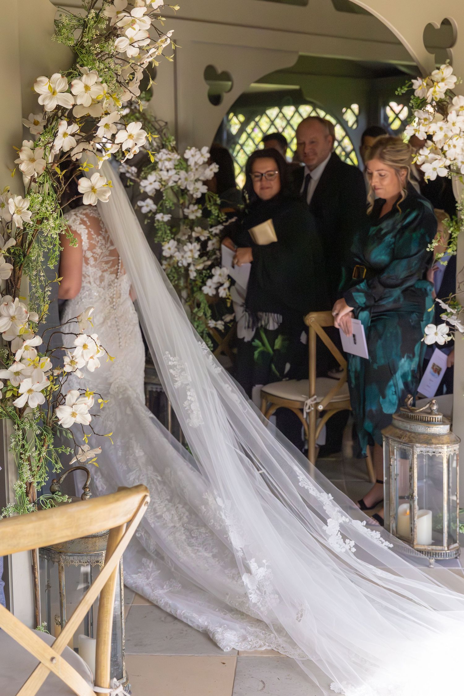 Wedding ceremony setup with white floral arrangements and decorative lanterns in an elegant archway.