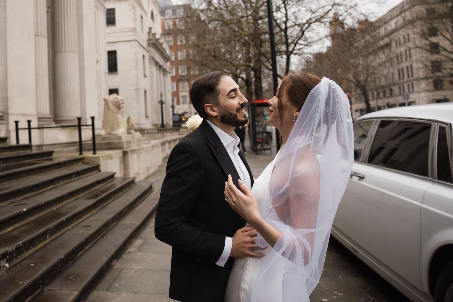 A bride and groom share a romantic moment on a London street, with the bride in a white veil and gown.