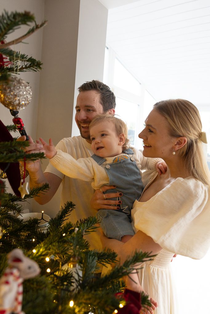 A family shares a happy moment while decorating their Christmas tree with ornaments and lights.