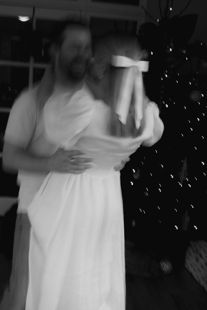 A couple embracing in a dimly lit room with a Christmas tree glowing in the background.