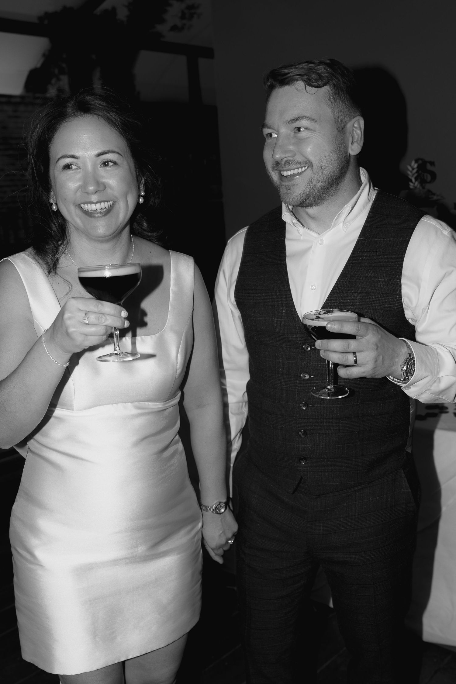 Black and white candid shots of wedding guests enjoying drinks and laughter at reception.