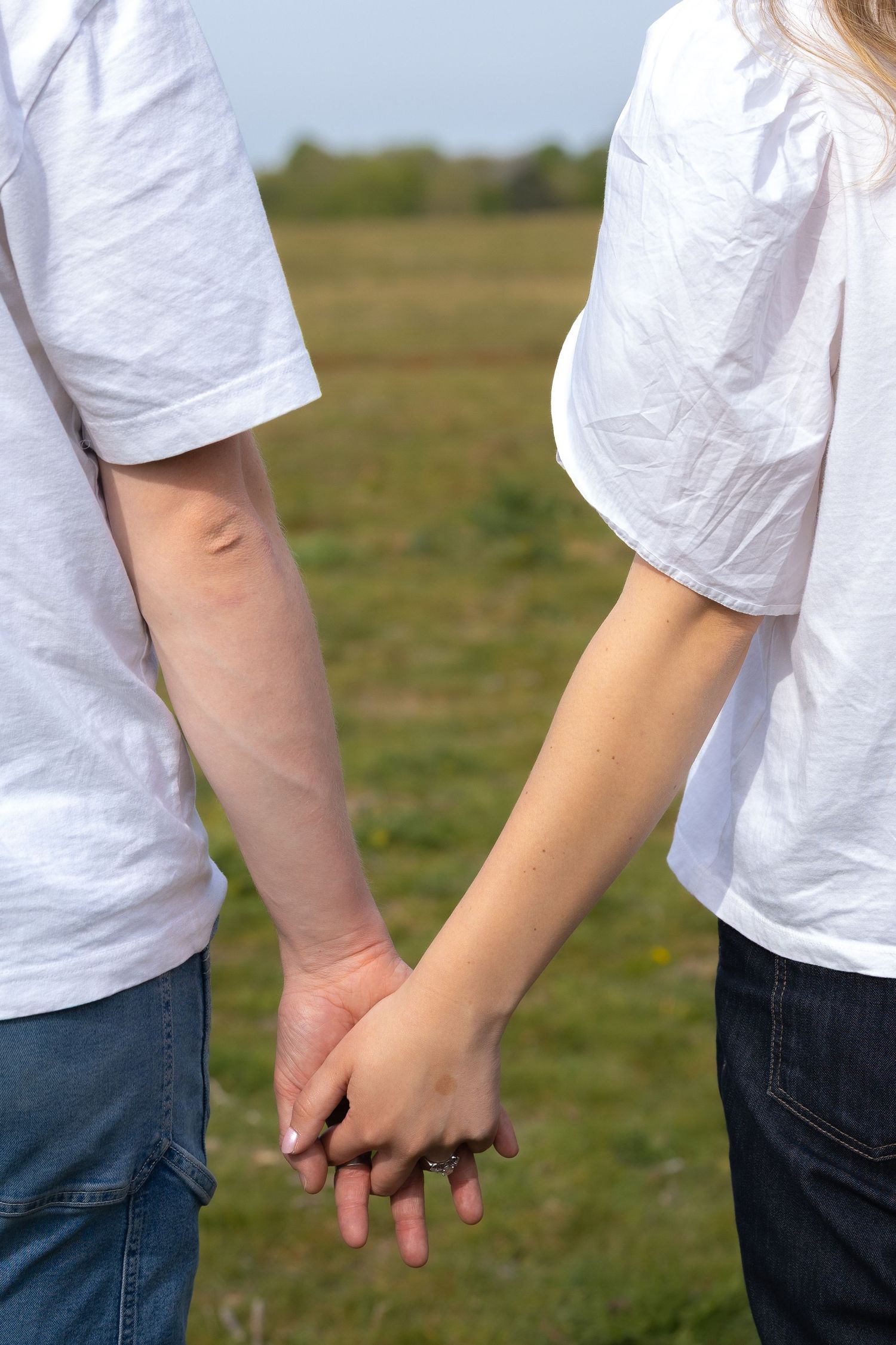Close-up of a couple holding hands in matching white t-shirts and jeans in a field.