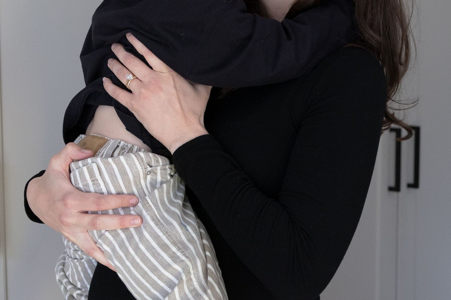 Mother in black long sleeve top tenderly holding newborn baby wrapped in striped blanket.