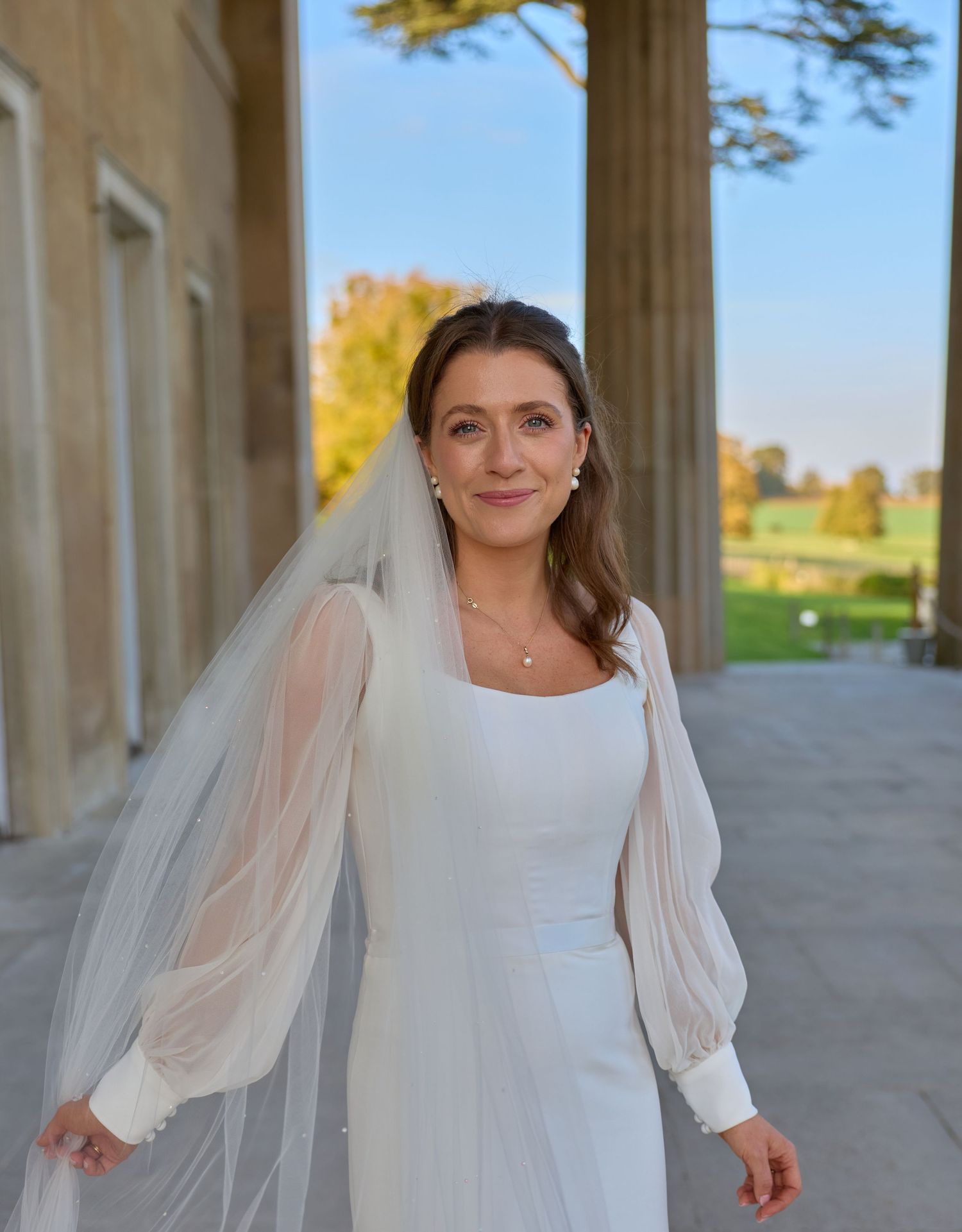 White bridal gown with delicate sheer sleeves captured in golden light among classical architecture.