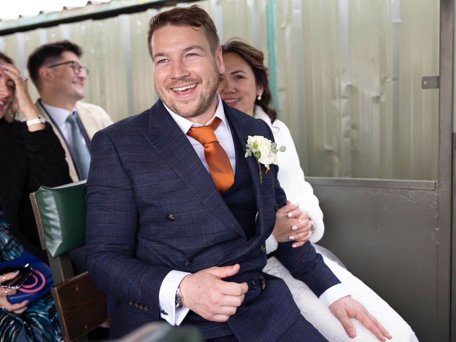 Wedding party members in navy suits with orange accents sharing laughs during celebration.