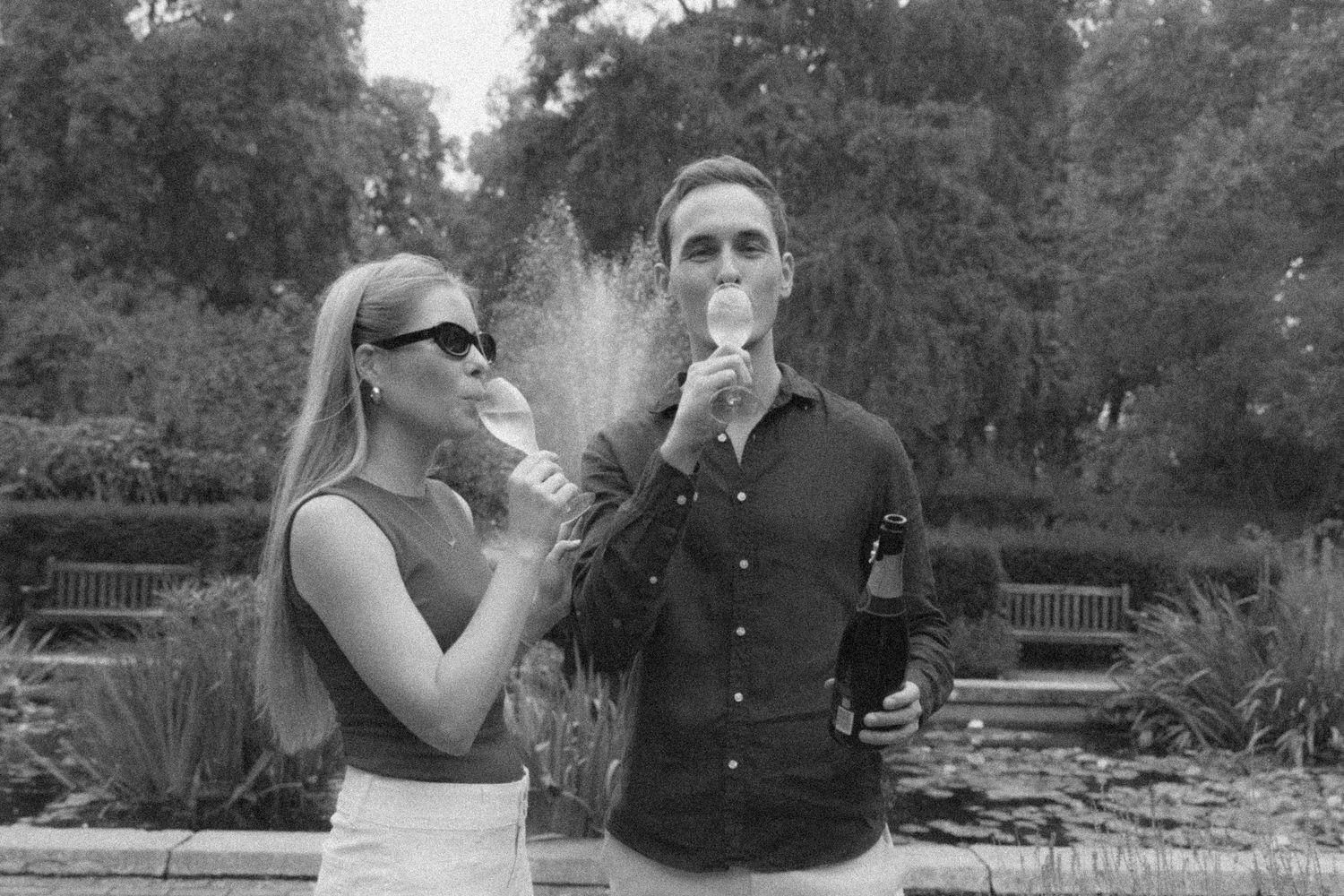 Black and white photo of a couple drinking champagne outdoors in a garden setting.