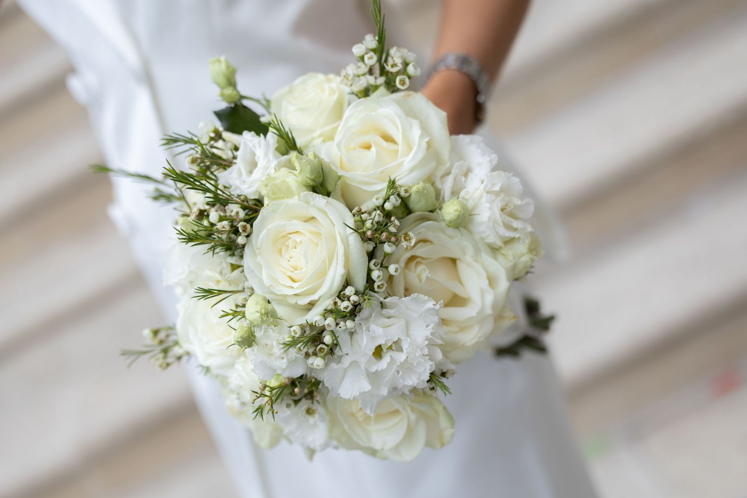 Bride holding a beautiful white wedding bouquet featuring roses, baby's breath, and lush greenery in an elegant arrangement.