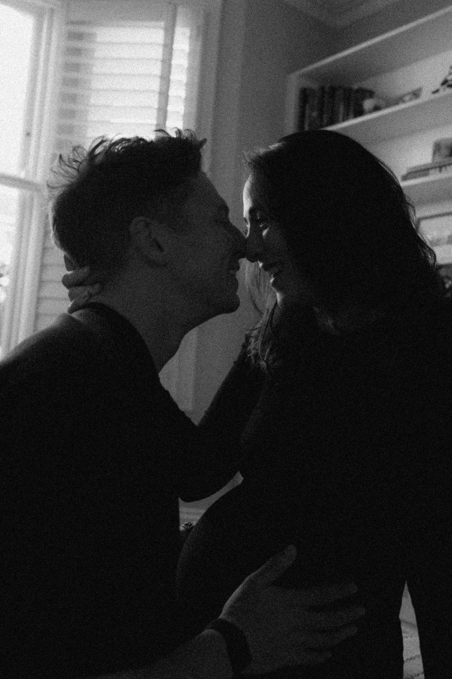 Black and white romantic photo of couple sharing tender moment near window indoors.