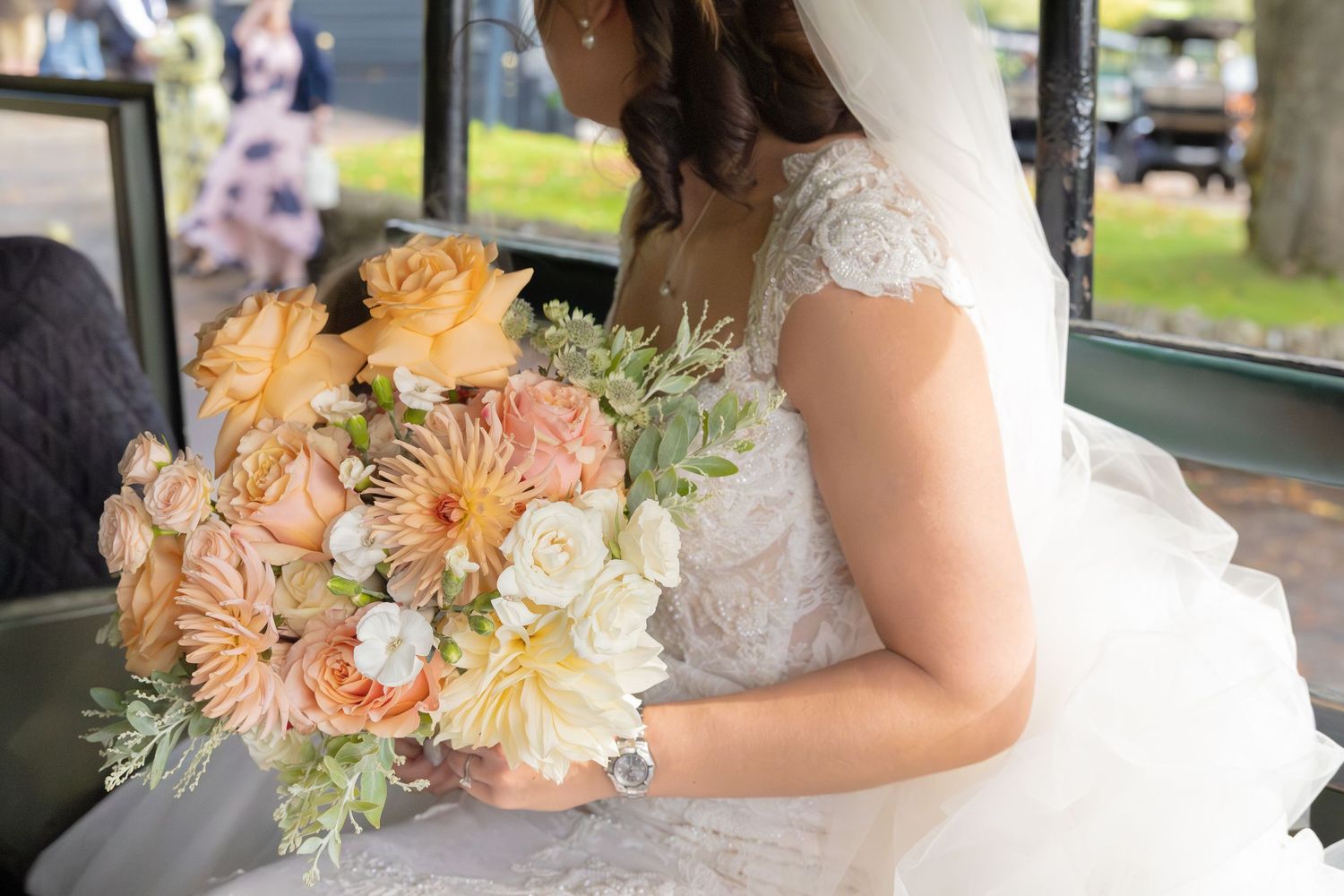 A peach and cream floral bouquet held by someone wearing a white lace wedding dress.