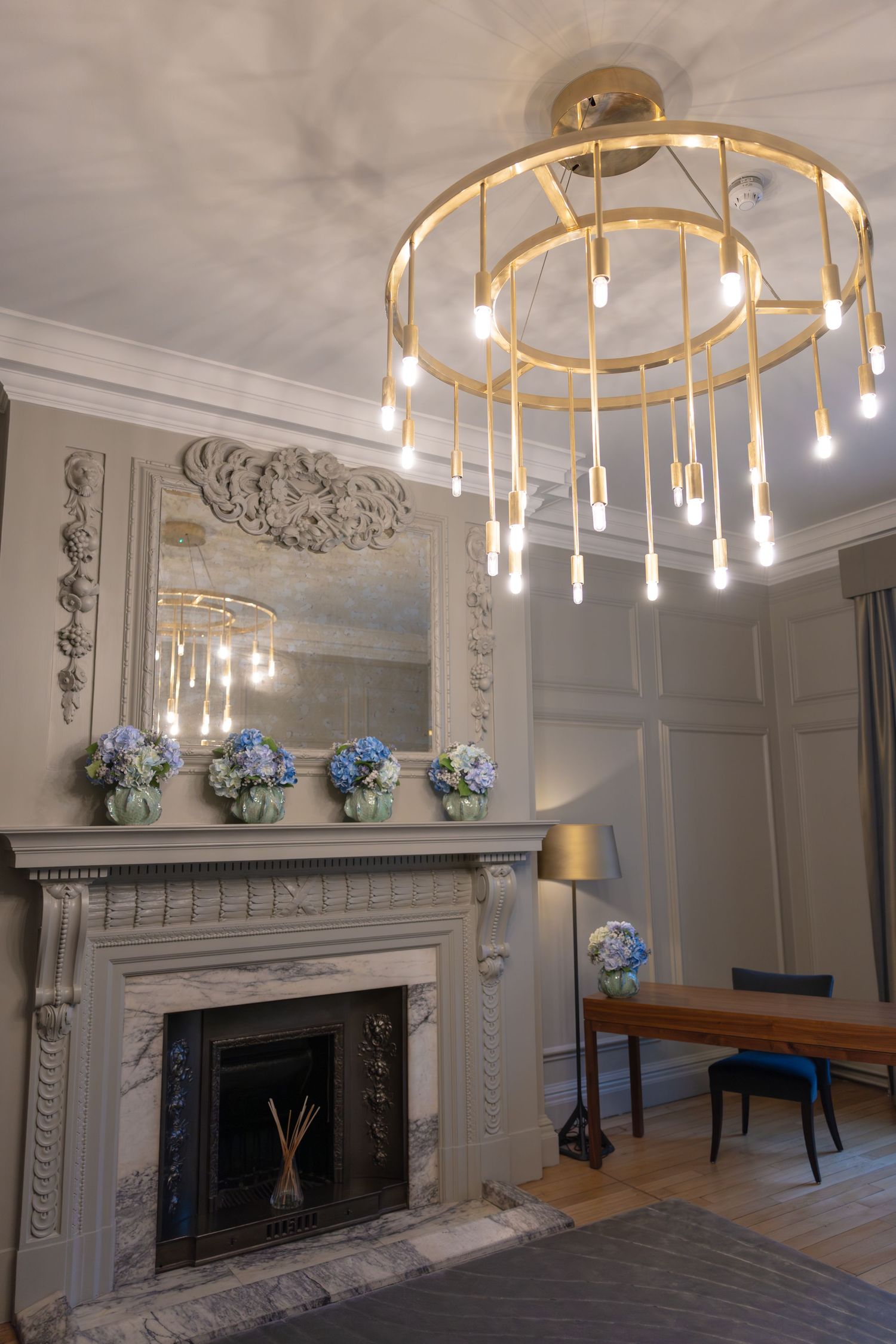 Elegant room with gold chandelier, ornate fireplace, and blue hydrangea floral arrangements.