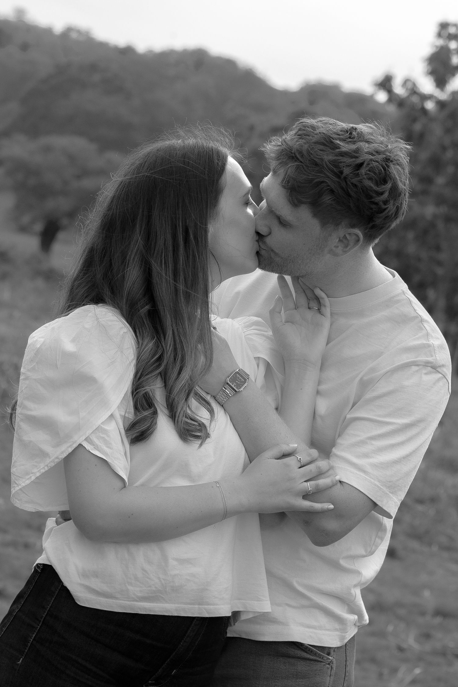 Couple sharing a romantic kiss outdoors in black and white engagement photo.