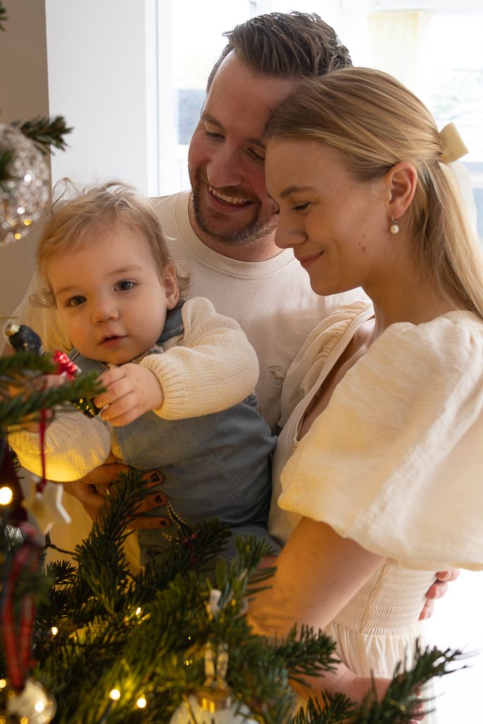 A cozy family moment as they decorate a Christmas tree with glowing lights and ornaments.