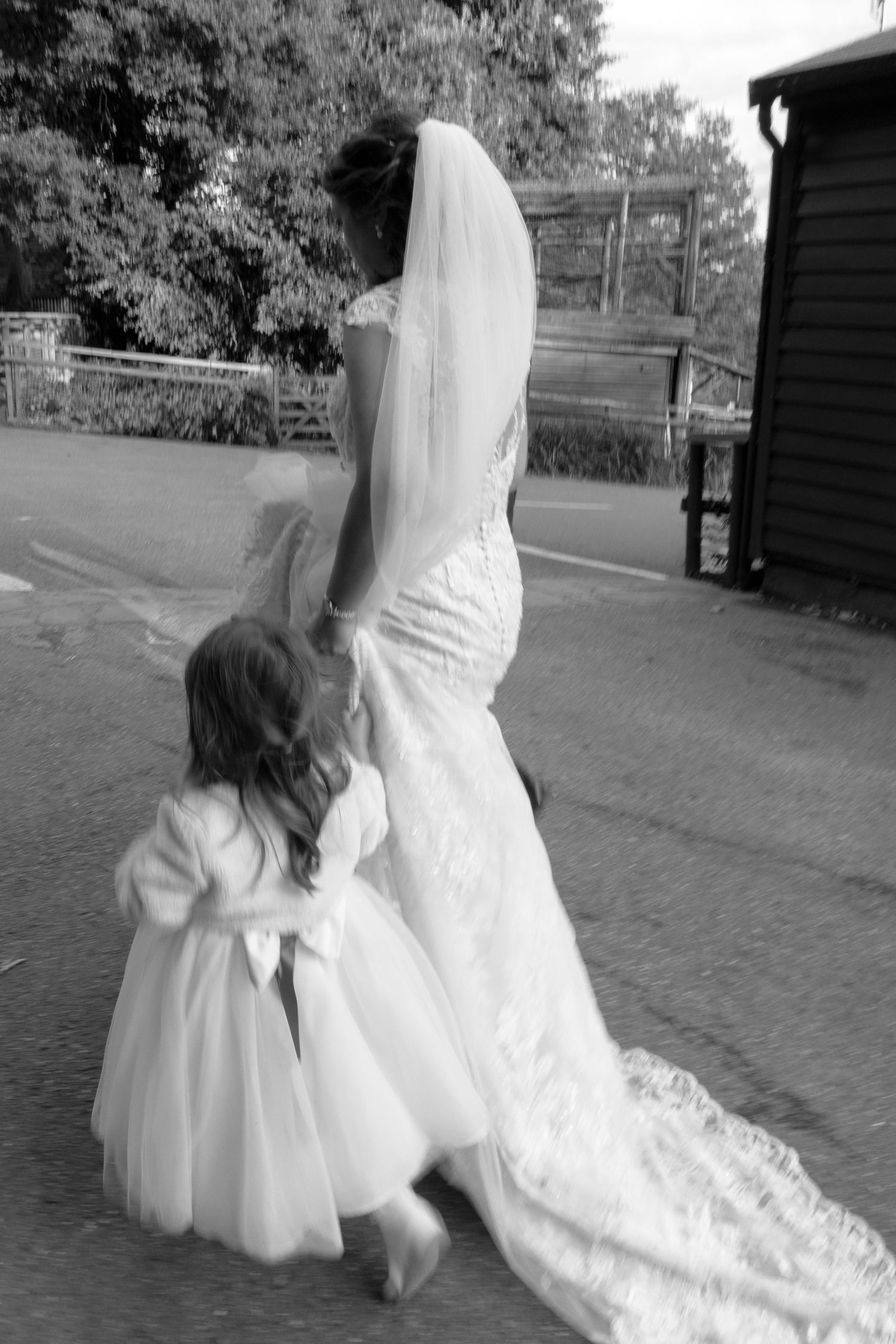 Black and white photo of wedding dress train and flower girl dress outdoors.
