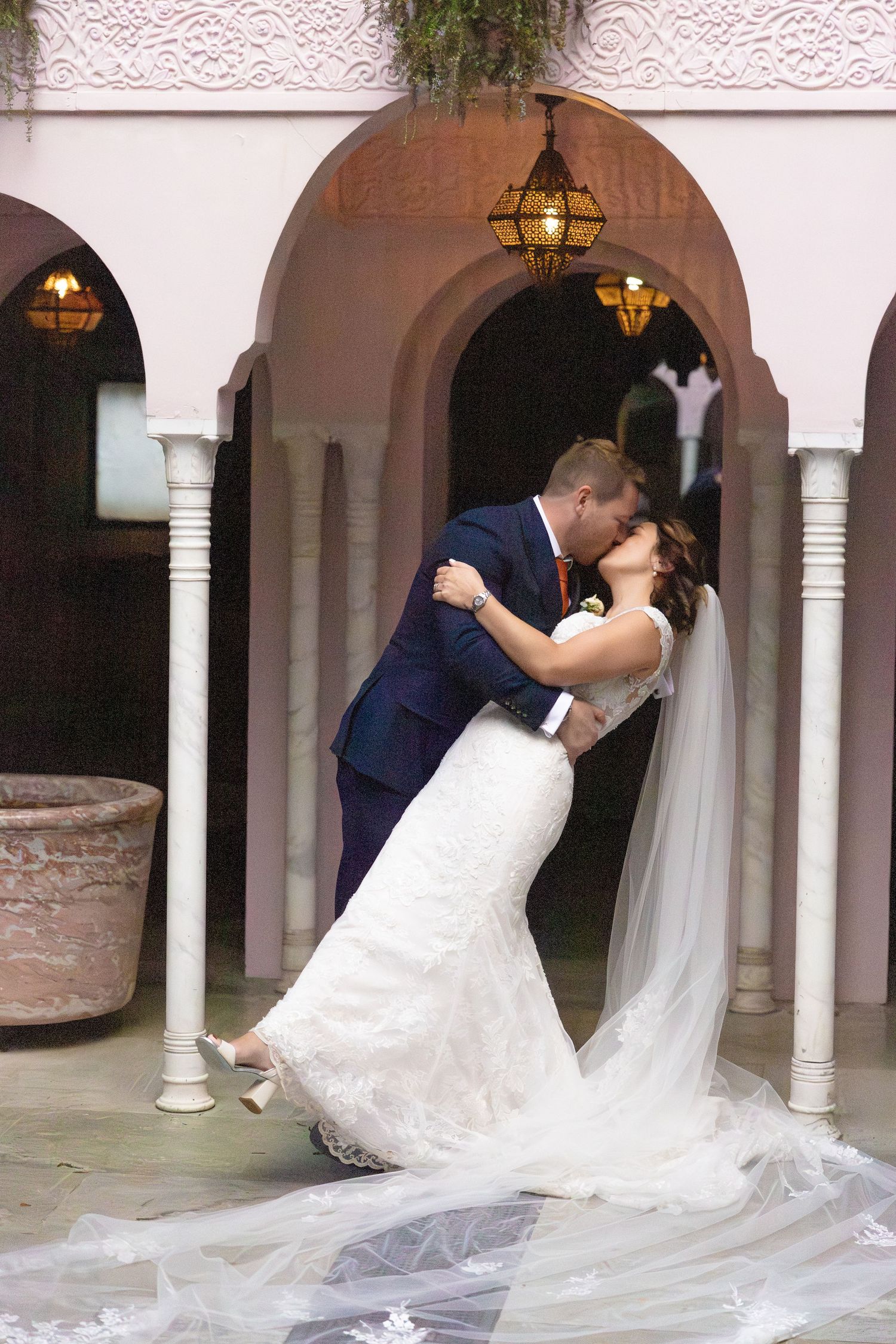 Wedding couple poses beneath elegant arched columns in a romantic architectural setting.