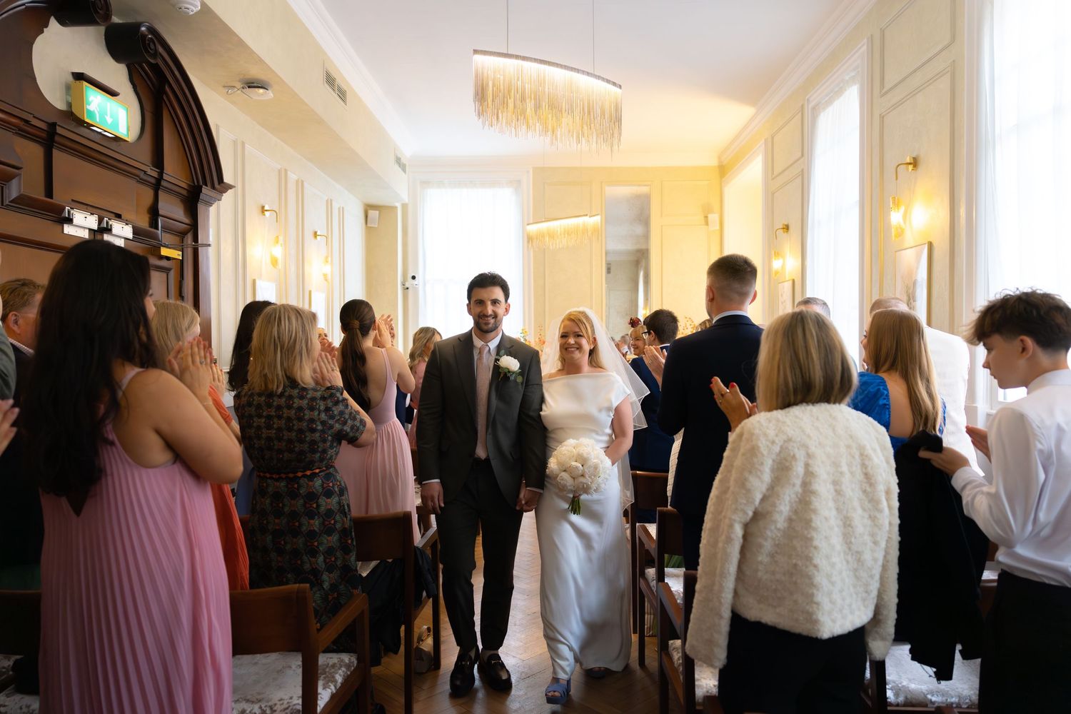 Bride and groom walking down the aisle at an elegant indoor wedding ceremony with guests standing on both sides.