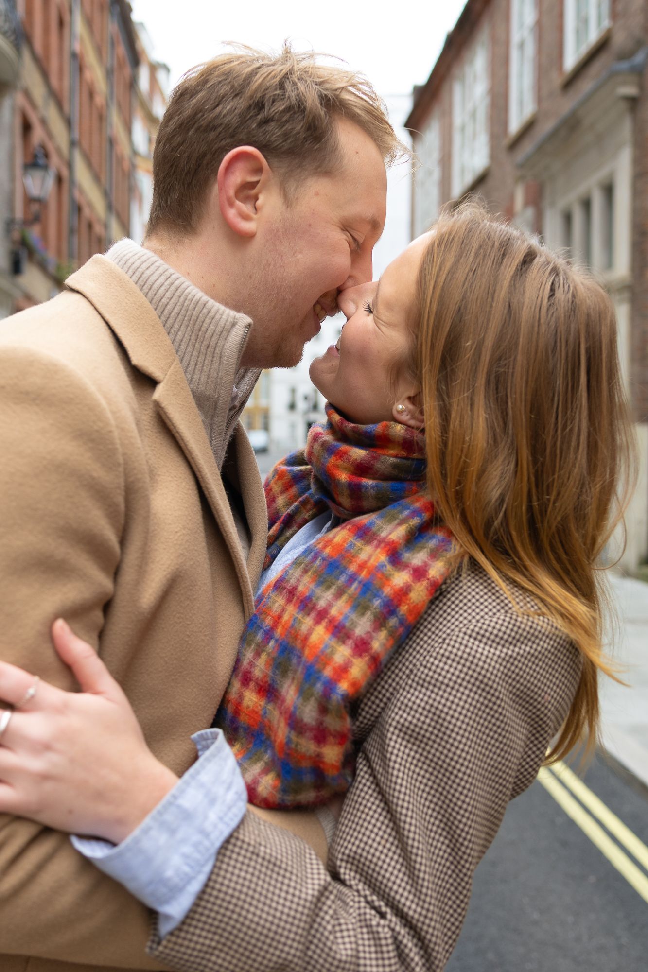 An intimate moment between a couple wearing scarves on an urban street.