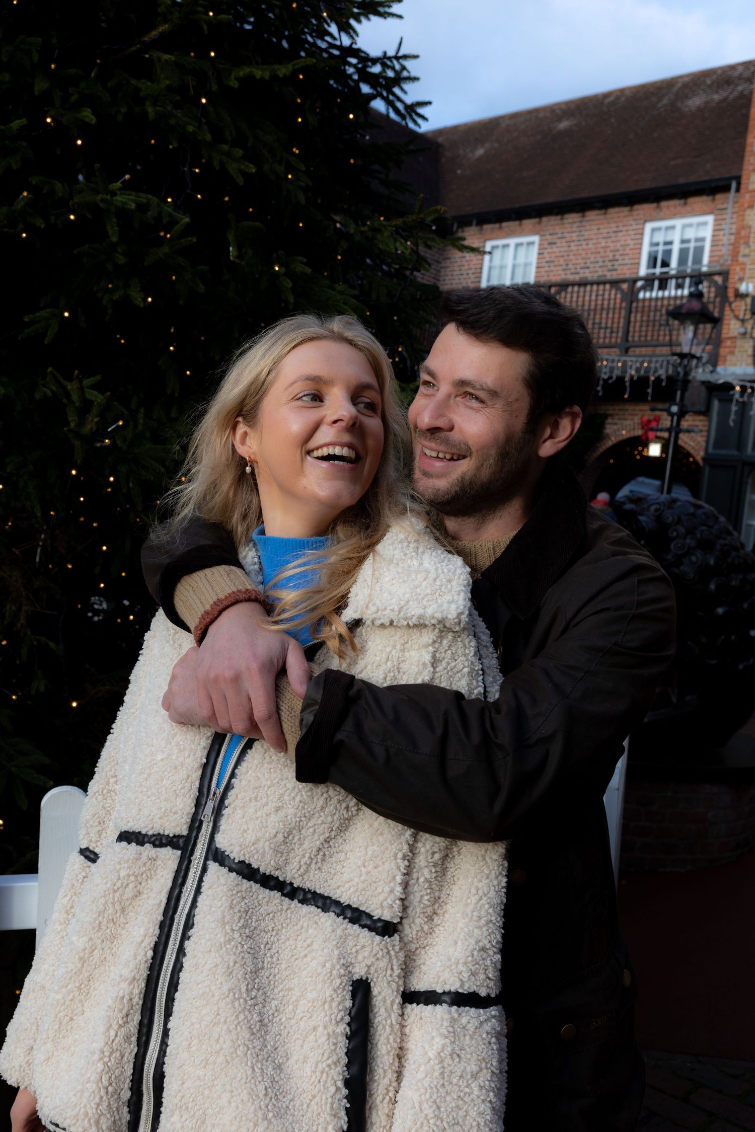 A couple shares a joyful moment together outdoors wearing winter coats during the holiday season.