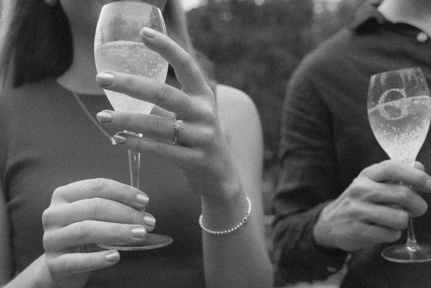 Black and white photo of two people holding wine glasses at a social event, woman wearing a bracelet and ring.