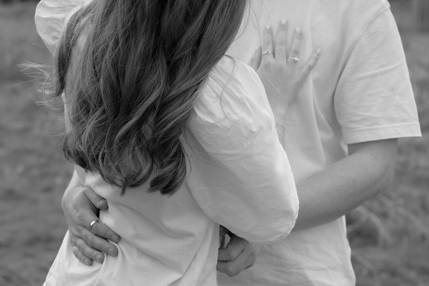 Black and white photo of a couple sharing a tender embrace outdoors in a field.