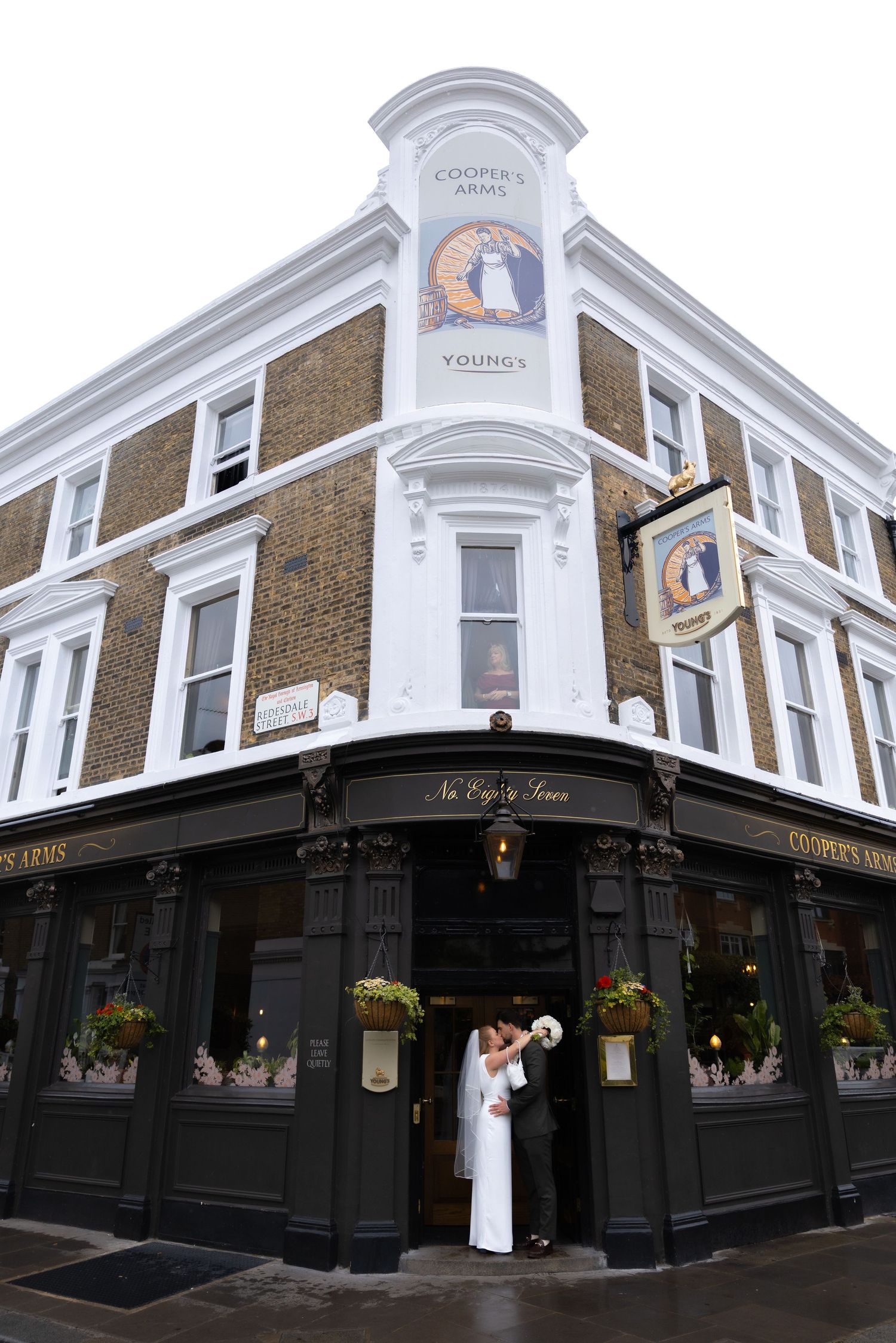 Bride and groom kissing outside Cooper's Arms Young's pub on their wedding day.