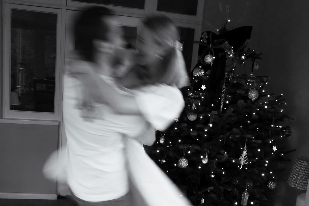 Motion-blurred dance movements captured in front of a glowing Christmas tree at night.