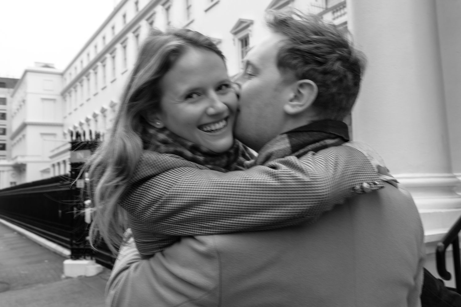A tender moment captured between a couple against white columns of a building.