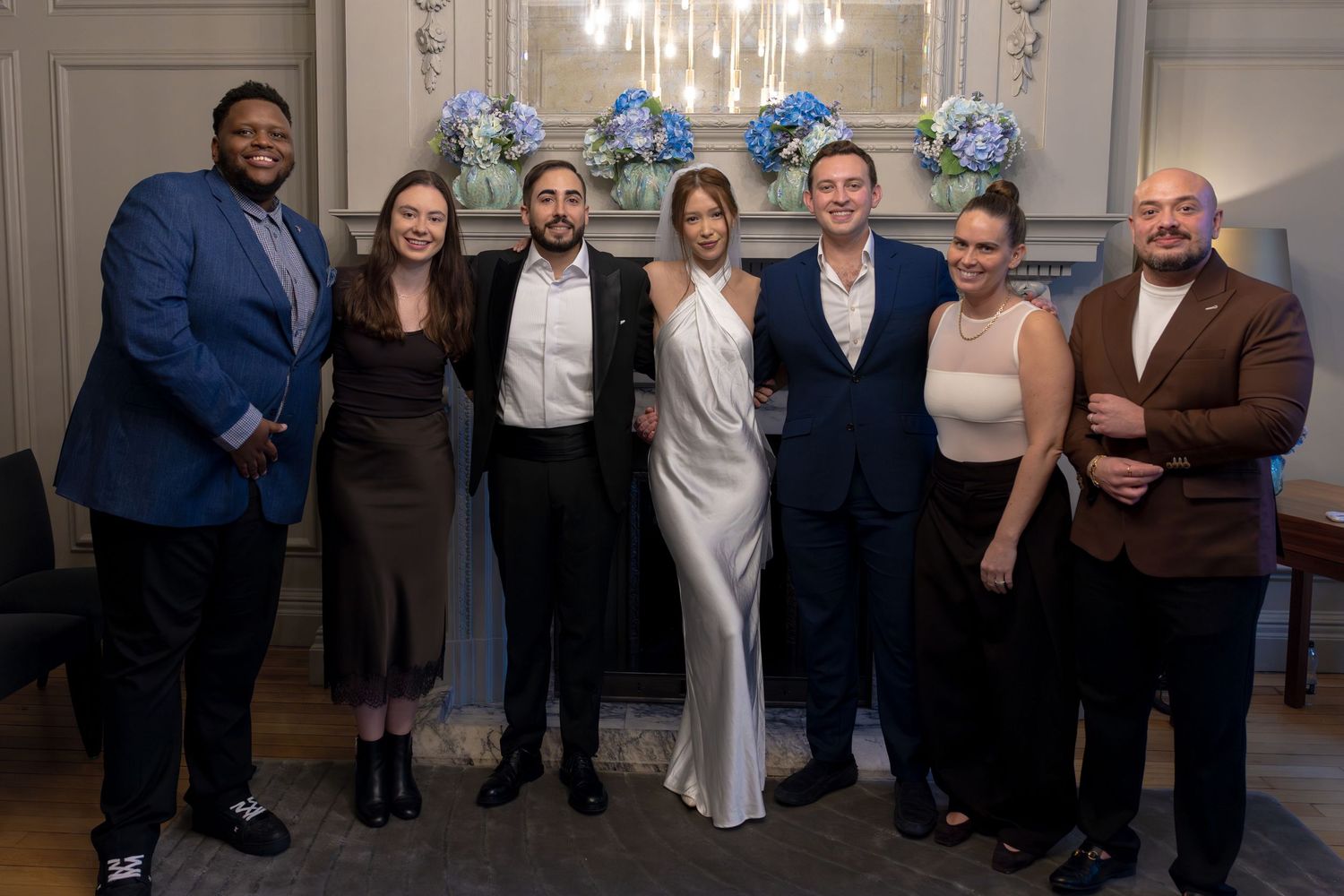 Group of seven people posing together at a formal event, with blue floral arrangements in the background.