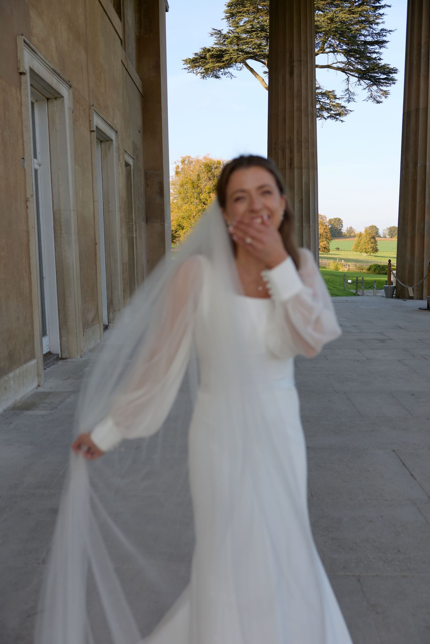 Joyful bridal moment captured in natural light among architectural columns.