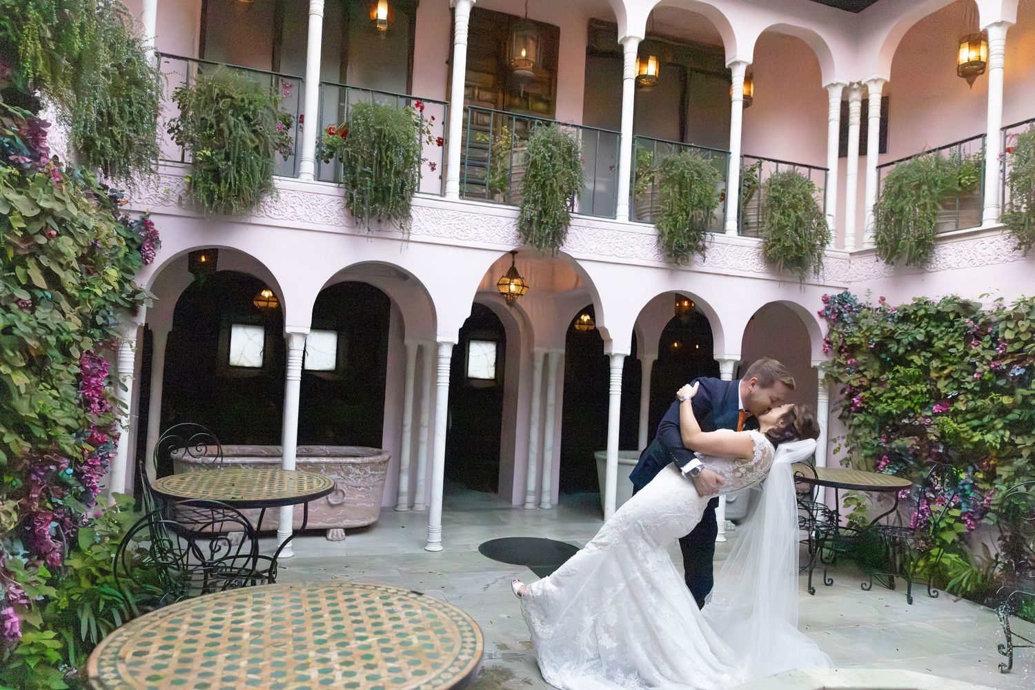 Wedding party walking through a beautiful pink-walled courtyard with arched columns.