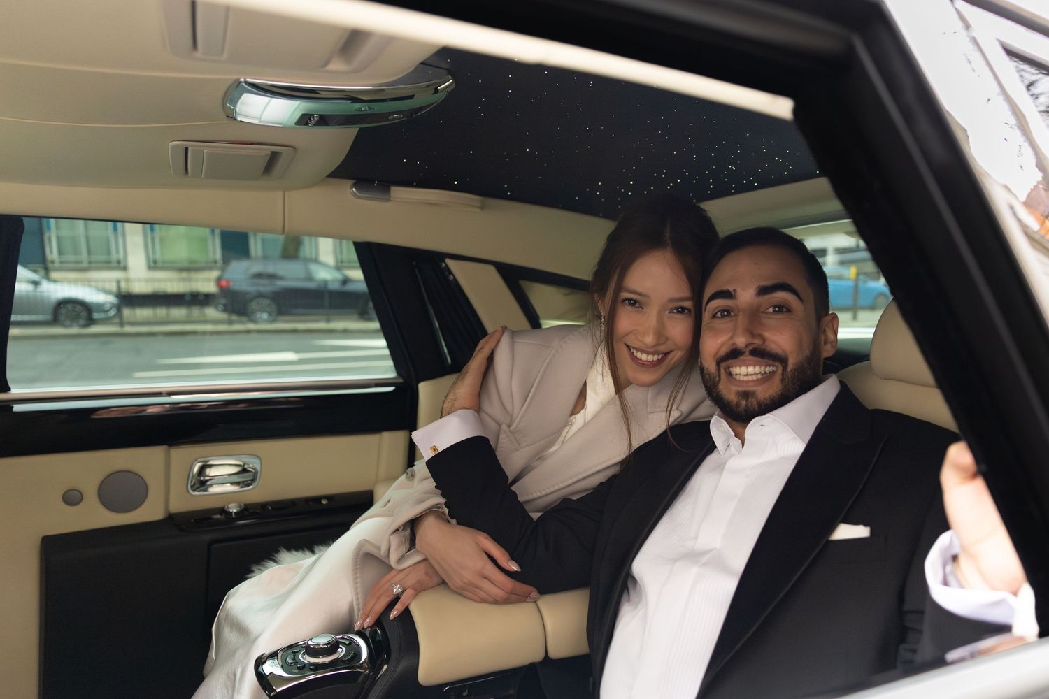 Smiling bride and groom sitting together in a luxury Rolls-Royce limousine on their wedding day.