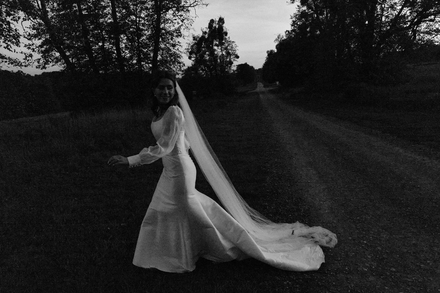 Black and white series capturing graceful movement of wedding dress and veil outdoors.
