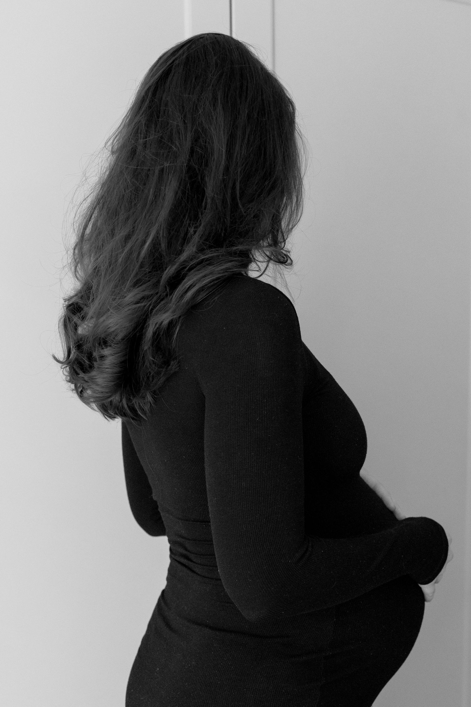 Black and white profile of pregnant woman in black dress showing baby bump.