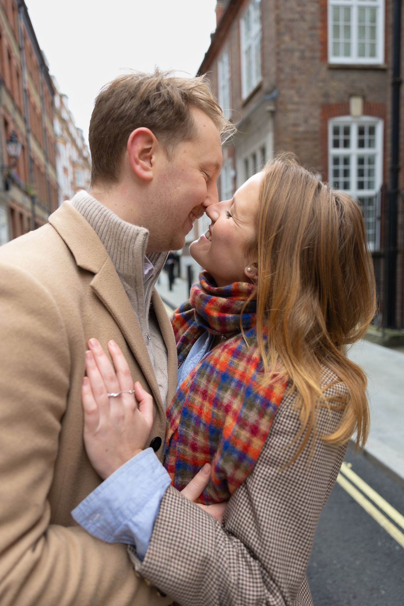 A couple shares a romantic moment on a brick-lined street in winter attire.