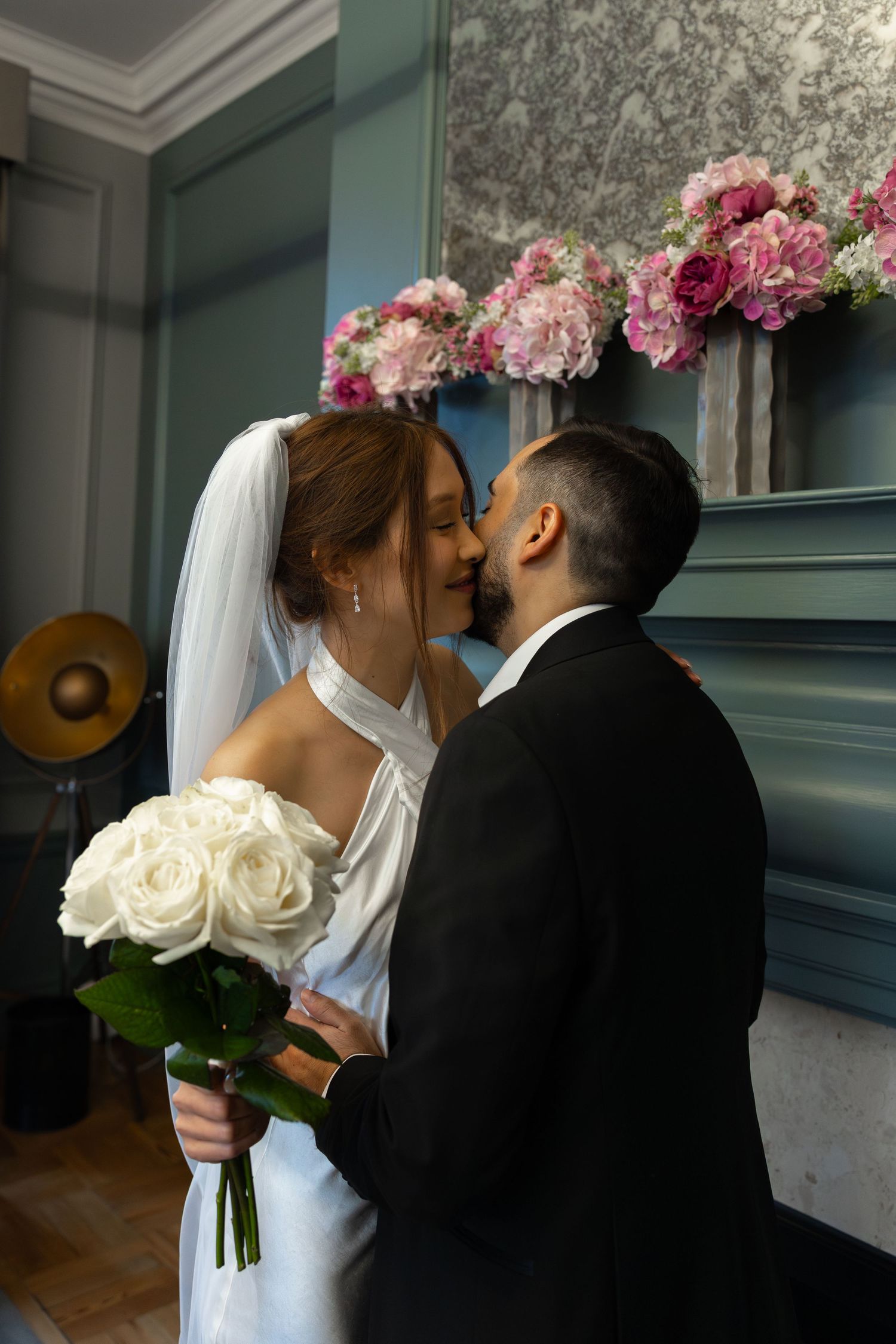 Bride and groom sharing a kiss at their wedding ceremony with pink floral arrangements in the background.