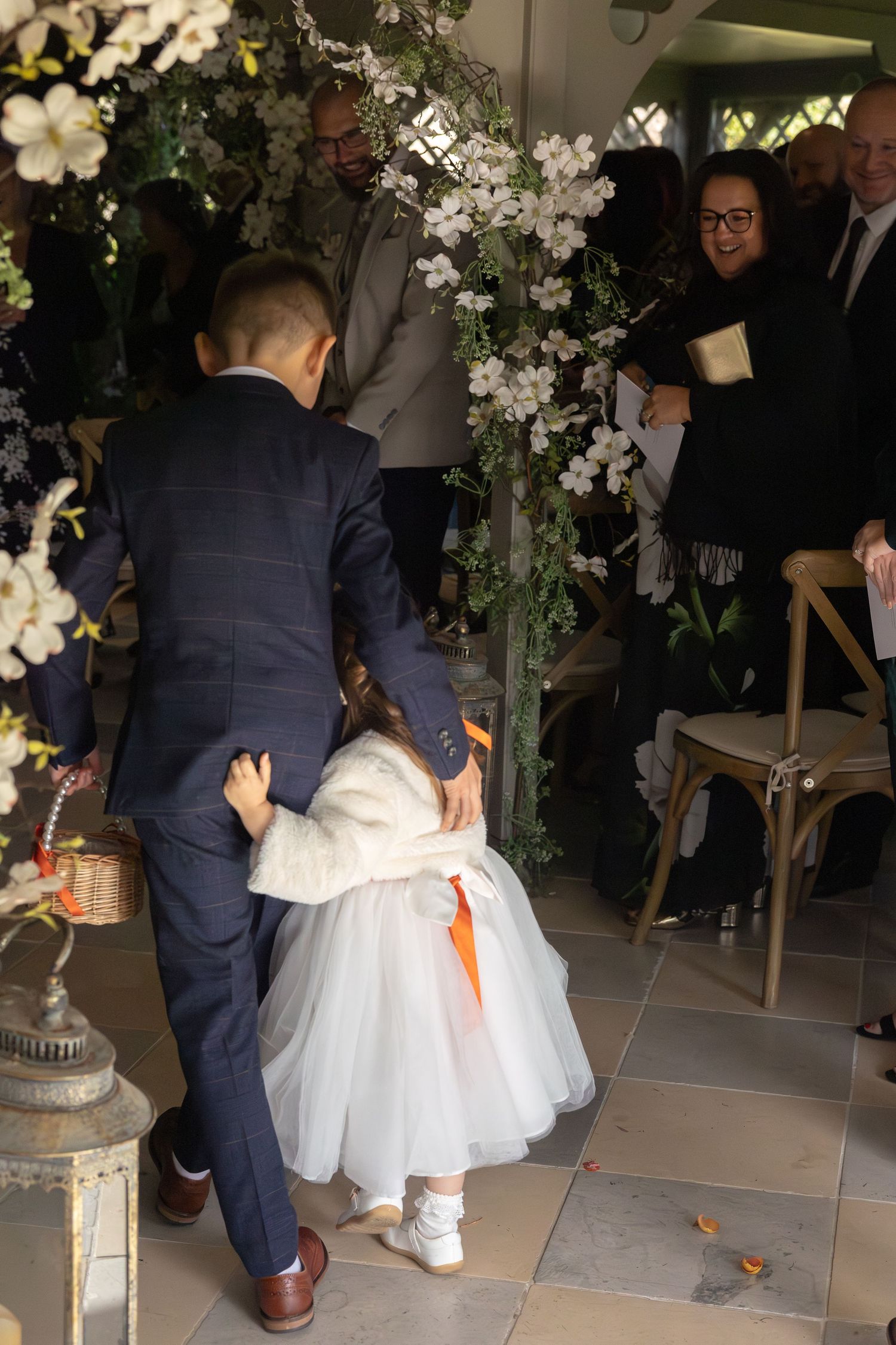 Wedding couple kneels together under floral arch decorations during intimate ceremony.