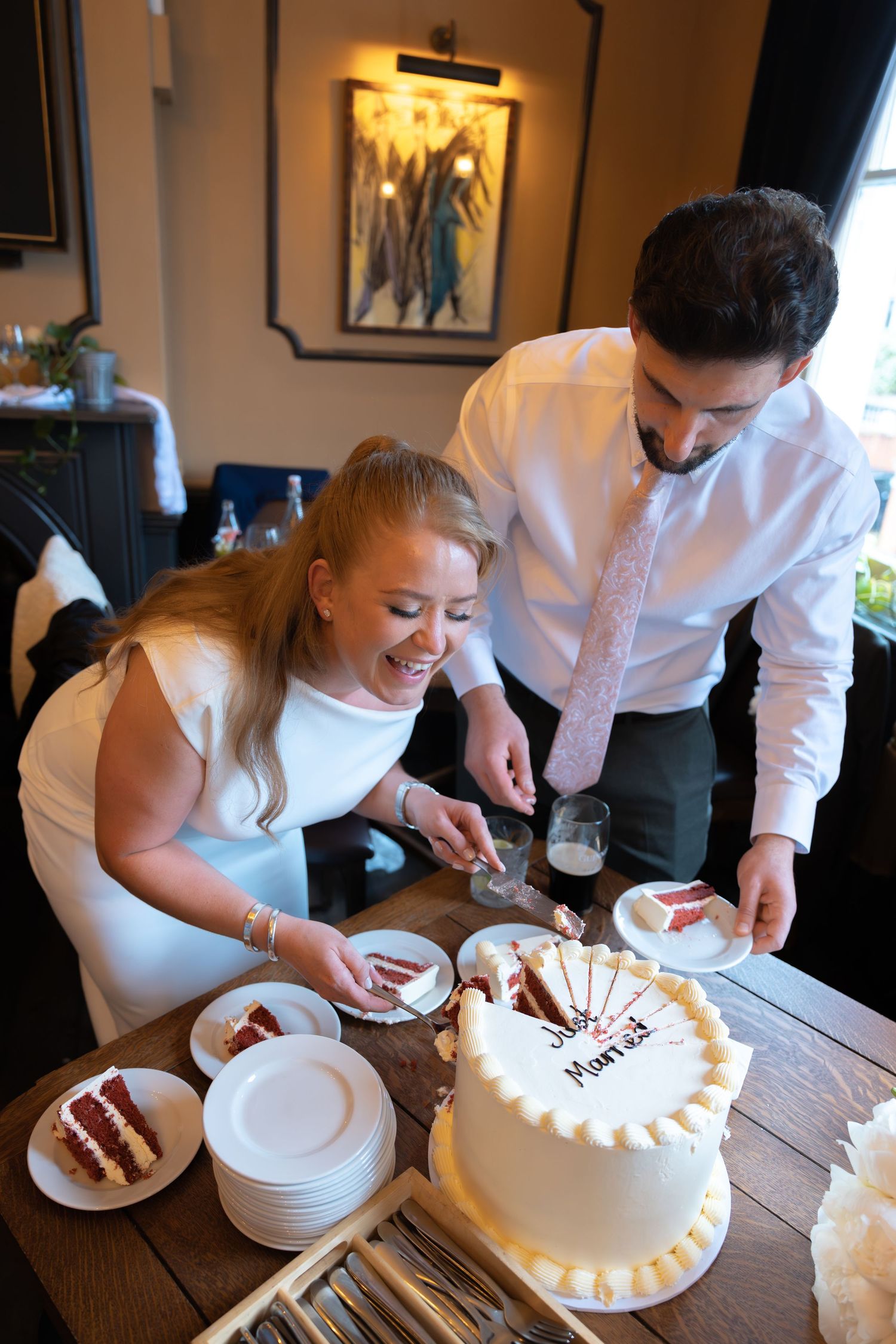 Smiling bride and groom cut white wedding cake together at reception table with red velvet cake layers inside.