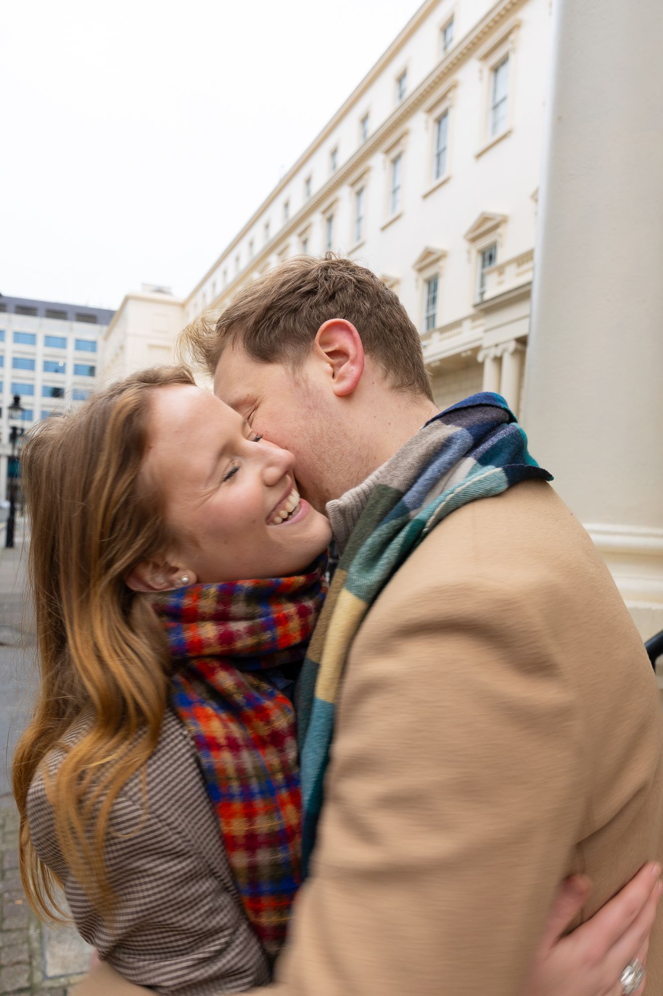 A couple shares a joyful embrace wearing winter attire on an urban street.